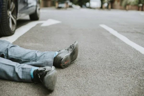 Injured pedestrian lying on a road beside a car
