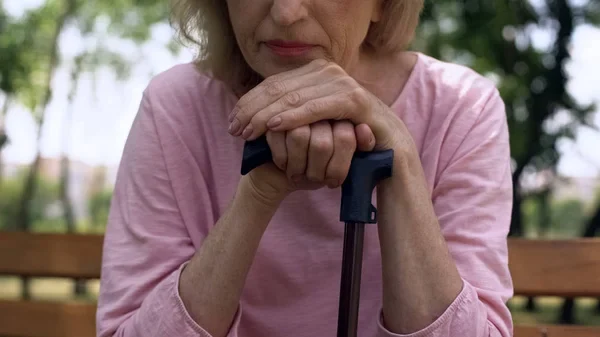 Older woman resting her hands on a walking cane