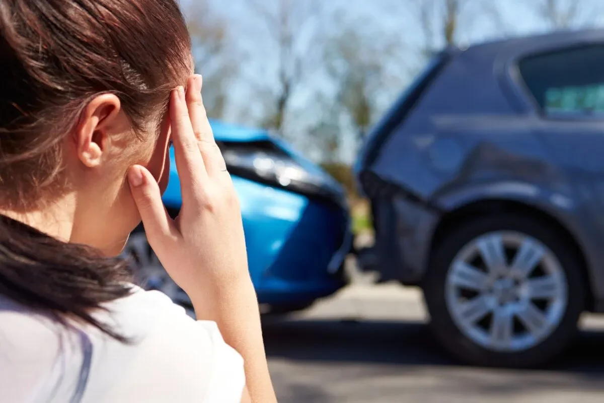 Woman holding her head beside damaged cars